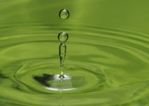 Wassertropfen fällt ins grüne Wasser und erzeugt Wellen