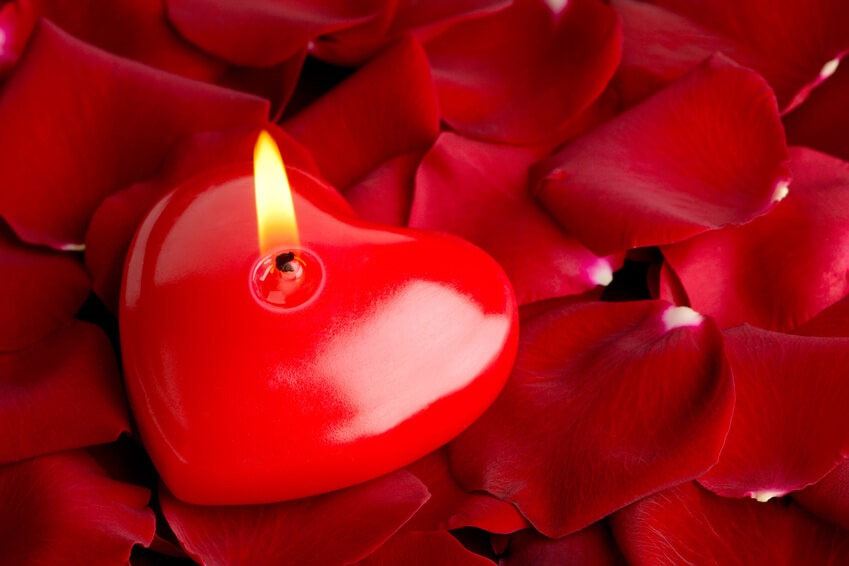 Rote Herzkerze mit brennender Flamme auf roten Rosenblättern