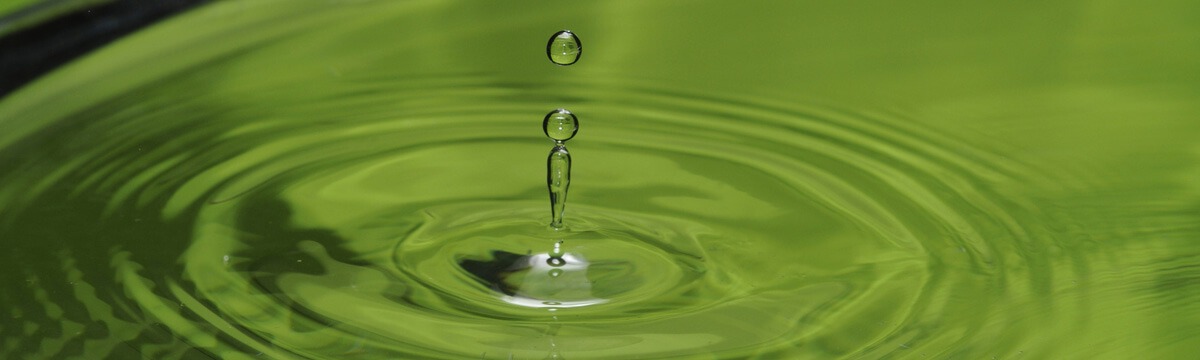 Wassertropfen fällt ins grüne Wasser und erzeugt Wellen