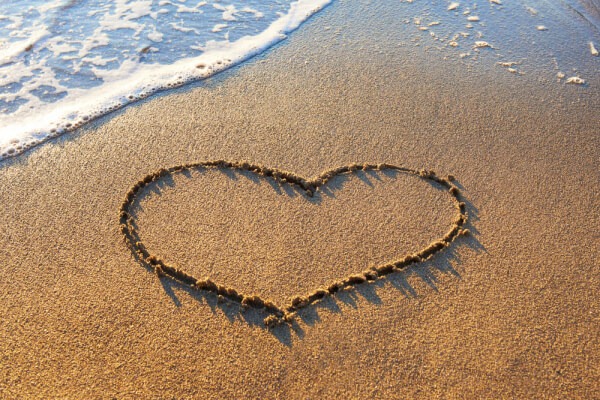 Herz in den Sand am Strand gezeichnet, dahinter die Brandung