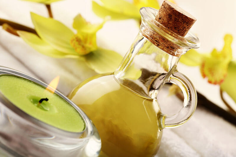 Massageöl in einer Glaskaraffe mit grüner Kerze und gelber Orchidee