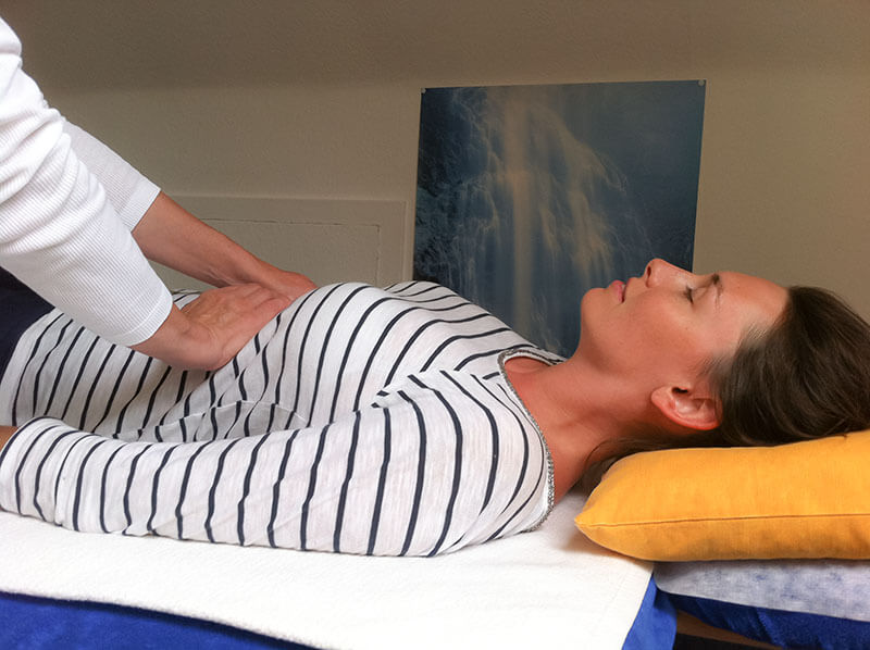Reiki-Behandlung: Hände liegen sanft auf dem Bauch einer Frau auf der Massageliege
