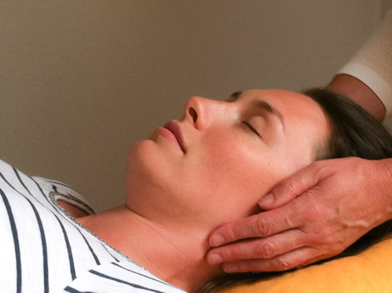 Reiki-Behandlung: Hände halten Kopf und Nacken einer entspannt liegenden Frau