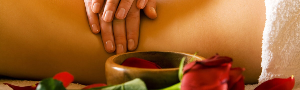 Hände bei der Rückenmassage, davor Holzschale mit roten Rosenblättern